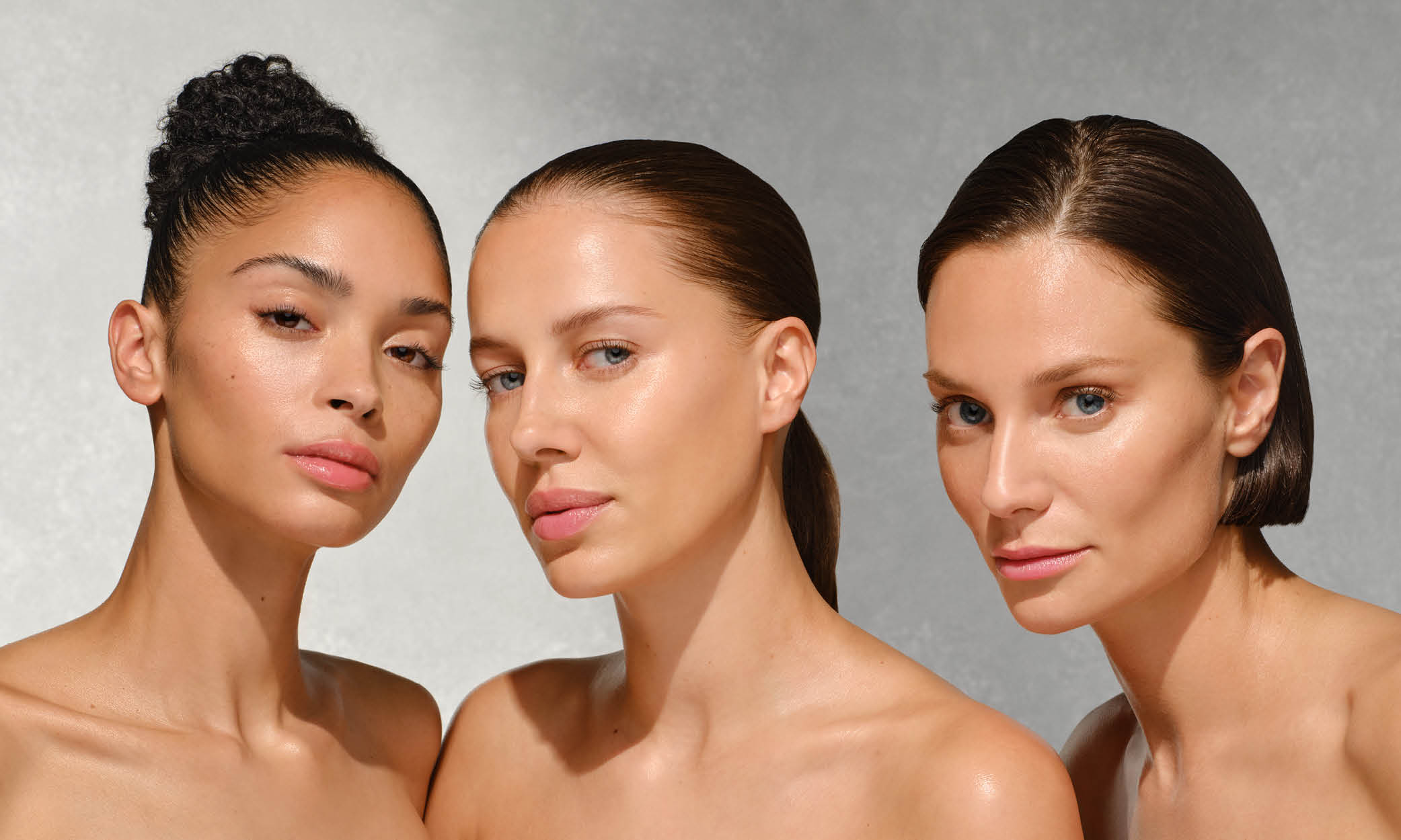 Drei Frauen Schulter an Schulter vor grauem Hintergrund